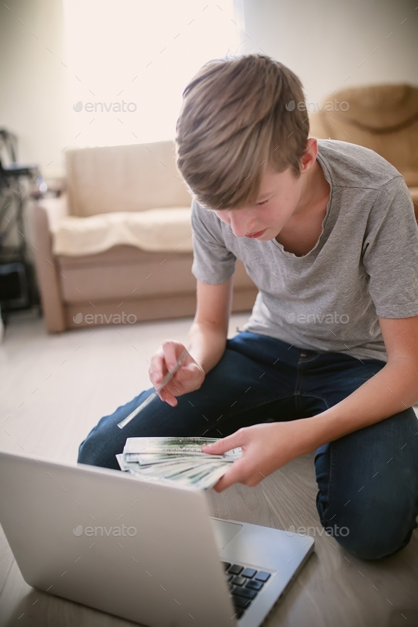A teenager holding a fan of dollar bills in his hands. The boy shows cash in webcam. Online money