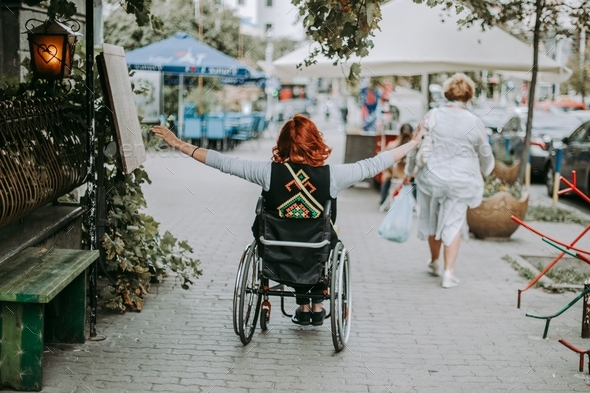 Happy young woman in a wheelchair rides around the city with arms outstretched to sides. Freedom