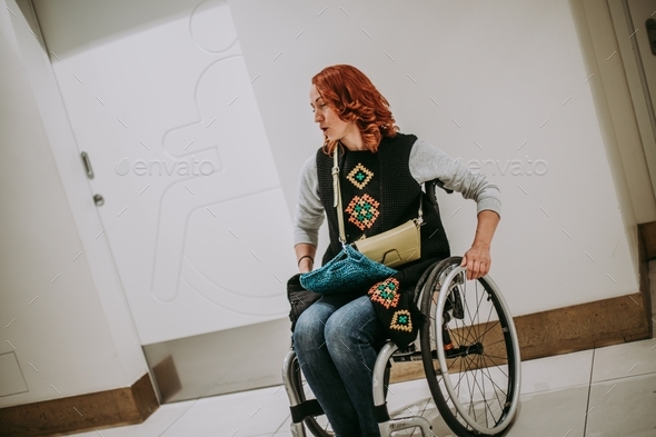 woman in a wheelchair near washroom door with a toilet sign for people with disabilities.