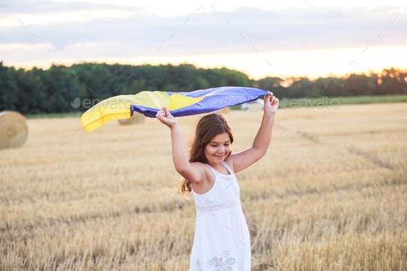 girl with waving flag of Ukraine runs across field of mown wheat on Independence Day of Ukraine