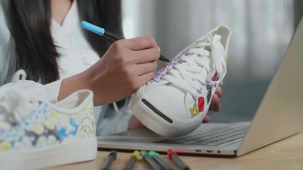 Close Up Of Female Footwear Designer'S Hands Putting Coloured Unique Patterns On Sneakers At Home alt