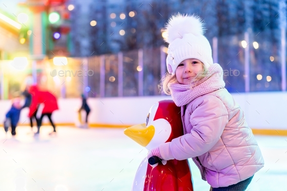 A little girl skates on an ice rink holding on to the support, teaching children to skate