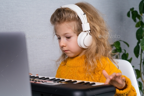 A little girl in white headphones learns music online, distance learning on a synthesizer