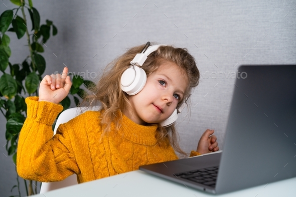 A little girl in white headphones learns music online, distance learning from home, technology