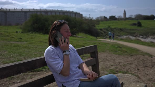 The Girl Talks on the Phone Sitting on a Bench and Looking at the Sea alt