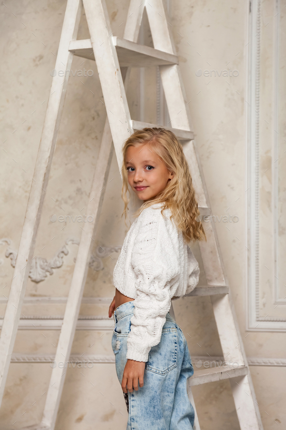 Little girl 6-7 years old blonde princess model in stylish clothe standing at stairs, posing