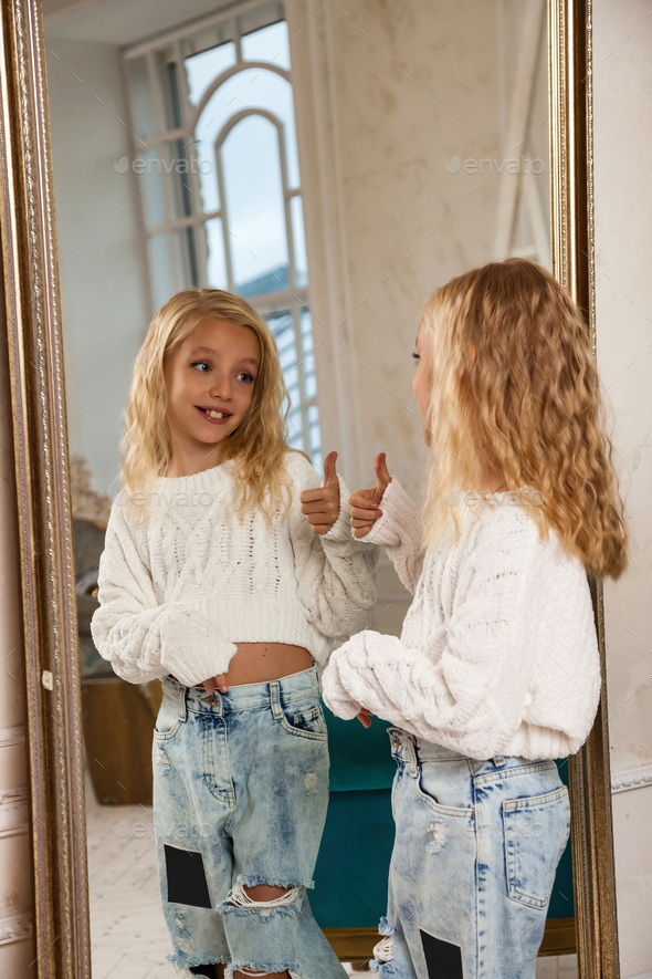 Little girl 6-7 years old blonde princess model in stylish clothe standing looking at reflection