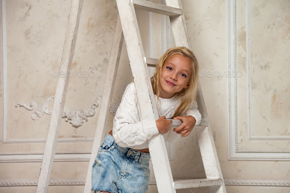 Little girl 6-7 years old blonde princess model in stylish clothe posing at stairs