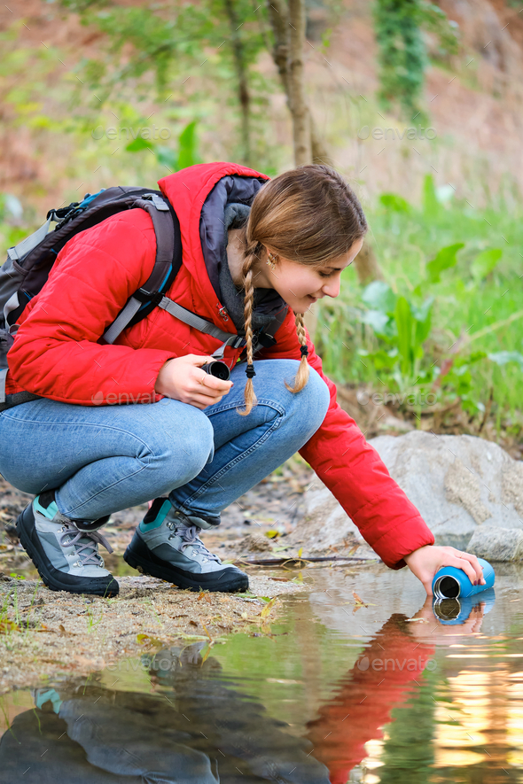 Trekker filling water bottle of raw water in a creek.