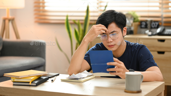 Stressed asian male frustrated with financial problems, managing household expenses at home.
