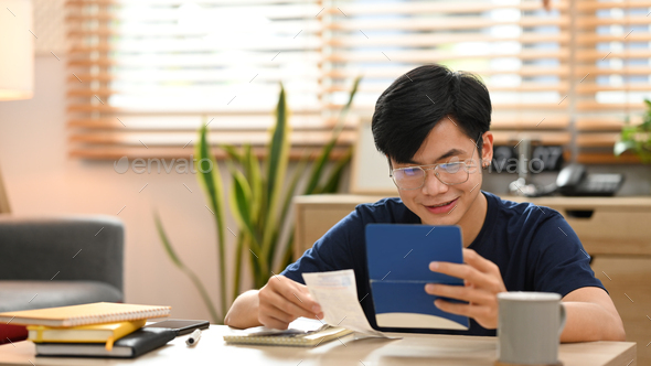 Smiling asian man managing household expenses expenditures, calculating money bank.