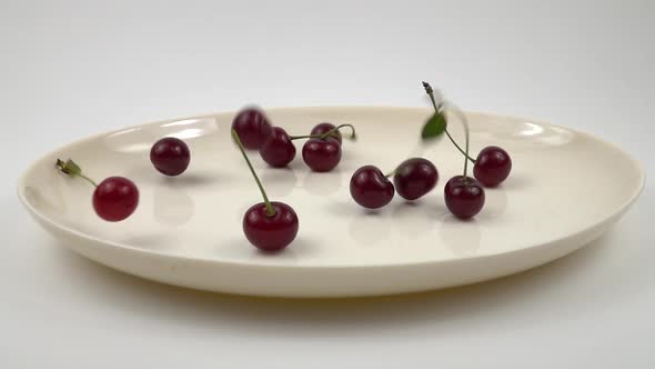 Ripe red cherries are laid out onto a white dish, slow motion
