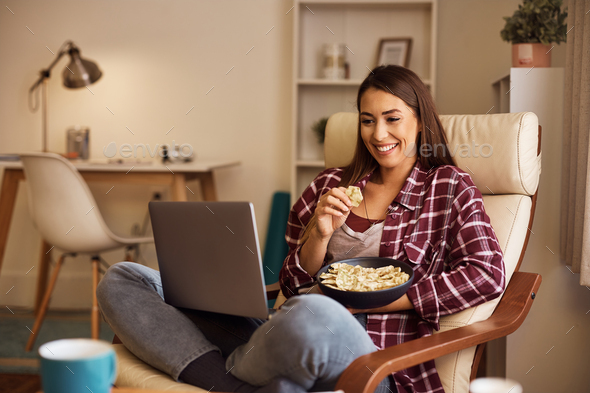Happy woman eating popcorn while binge watching on laptop at home. - Stock Photo - Images