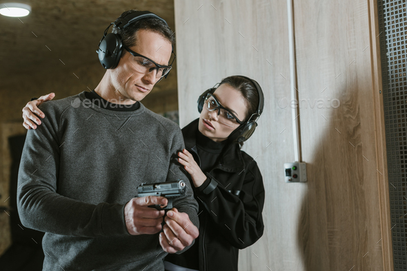 instructor helping client to stand with gun in shooting range