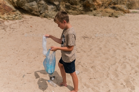 Young boy volunteer cleaning up litter on sunny beach. Garbage at the beach