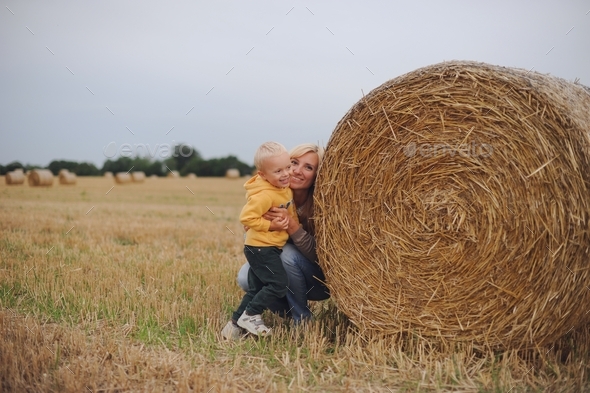 Mother and baby boy playing at the rural field between hay bales in summer