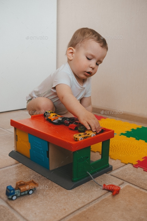 child in a white T-shirt plays multi-colored small cars and ikea parking on a bright carpet