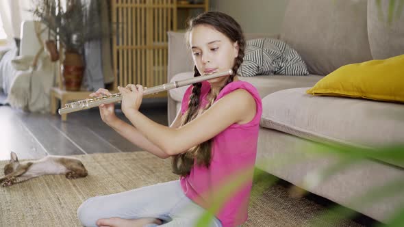 Little Girl Plays Flute on Floor at Home