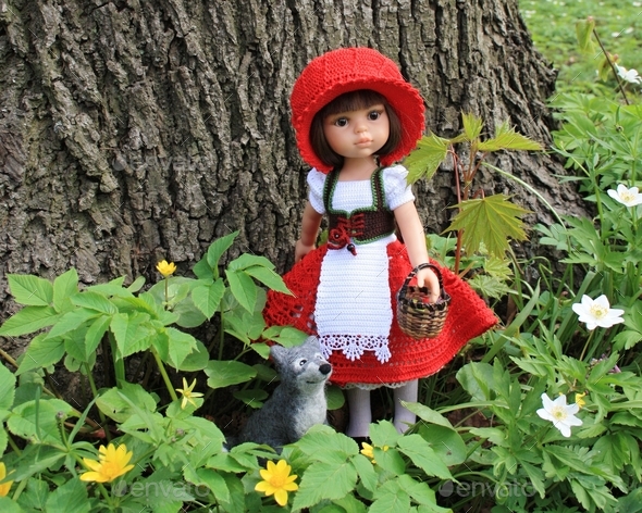 Doll dressed in handmade costume based on “Le Petit Chaperon rouge” fairy tale among spring flowers