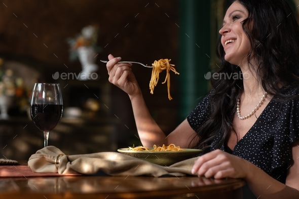 A beautiful young Italian woman eats spaghetti in an antique-style dining room