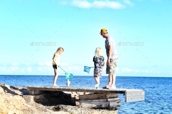 Father and kids crabbing and catching fish with nets on a jetty by the sea - Stock Photo - Images