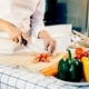 Woman using knife and hands cutting tomato on wooden board in kitchen room. - PhotoDune Item for Sale