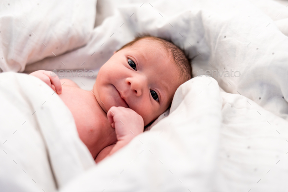 Calm newborn baby child lying in white bed sheets - Stock Photo - Images