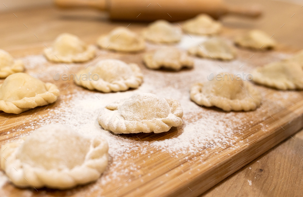 Raw dumplings polish traditional perogies lying on wooden board in kitchen - Stock Photo - Images