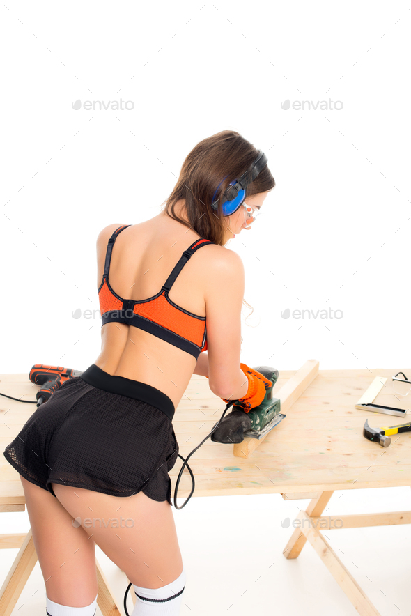 back view of girl in protective headphones working with grind tool at wooden table, isolated on