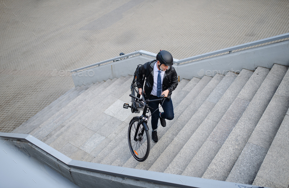 High angle view of businessman commuter on the way to work, carrying bike upstair, sustainable