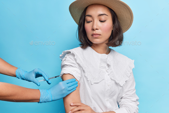 Serious Asian woman in white fashionable blouse hat gets coronavirus vaccine to feel protected looks