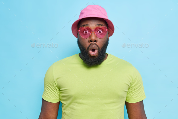Indoor shot of shocked Afro American man with thick beard keeps mouth opened and looks scared gasps