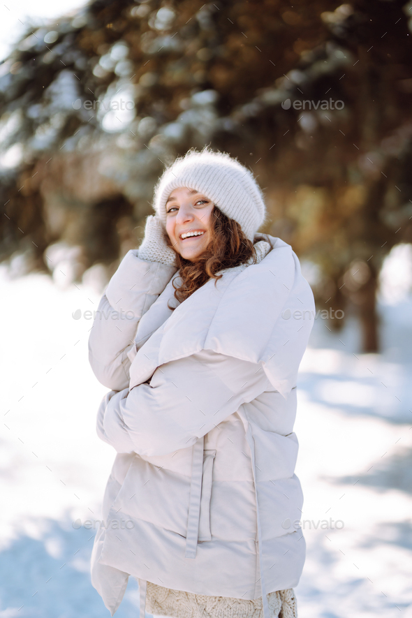 Young woman in winter style clothes walking in the snowy park