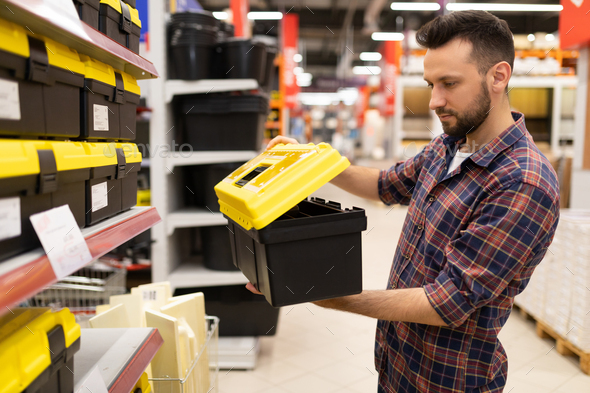 a male builder in a hardware store chooses a tool storage case