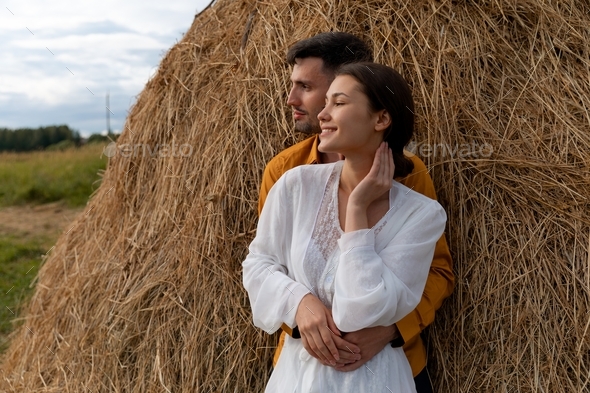 A couple stands next to haystack, love story and wedding inspiration
