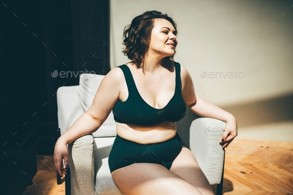 Plus size woman in beige underclothes pulling shapewear panties