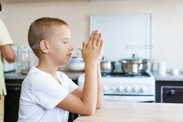 Caucasian boy prays at home at the table before eating. Stay home and pray