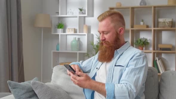 Addicted to Technology Young Handsome Redhead Man Resting on Cozy Sofa Involved in Using Smartphone alt