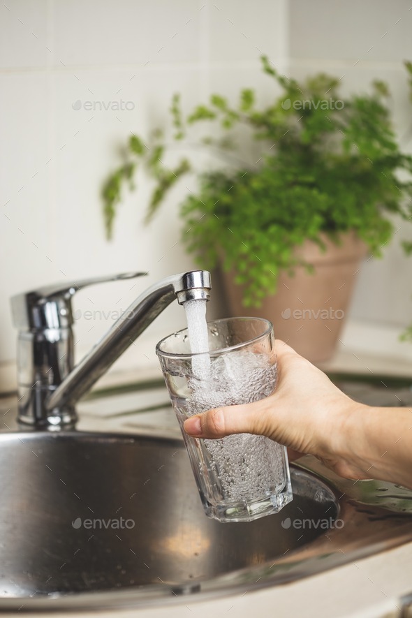 Clean tap water at home. Woman hand holding a drinking glass pouring it