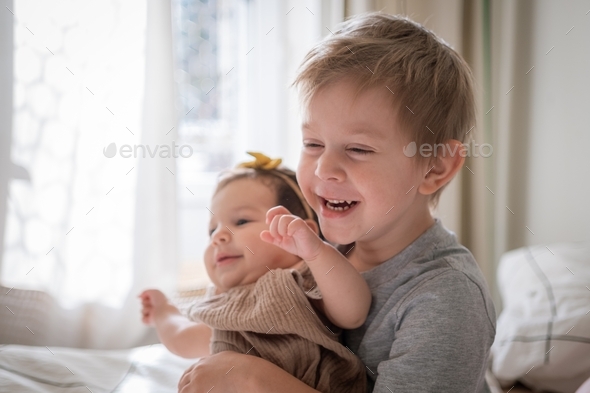 Toddler boy embarrassing his infant sister and laughing