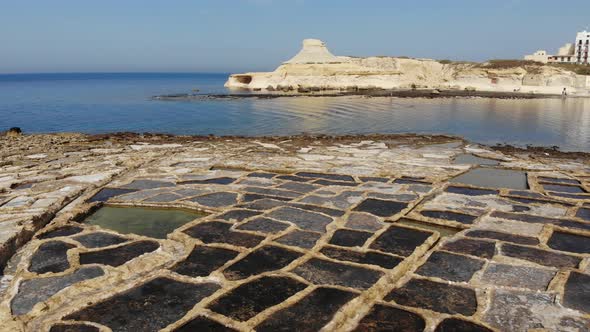 An aerial drone shot slowly pans across the rock-cut Salt Pans and beautiful coast of Gozo Island in alt