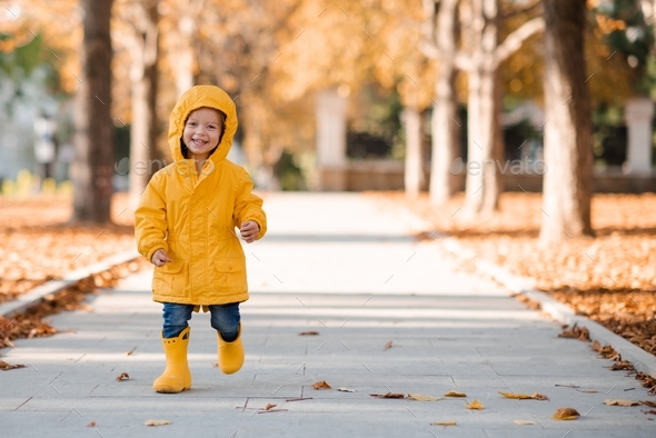 Smiling happy little girl wear yellow raincoat and rubber boots run in park. Happiness. Cheerful kid