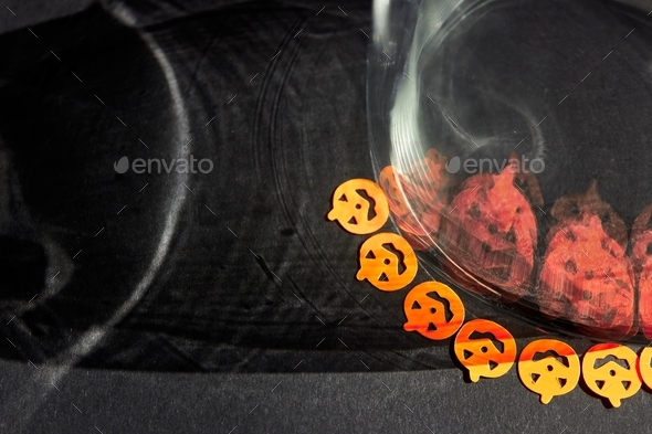 Bright orange little pumpkin stickers are reflected by big scary shadows in a glass glass.