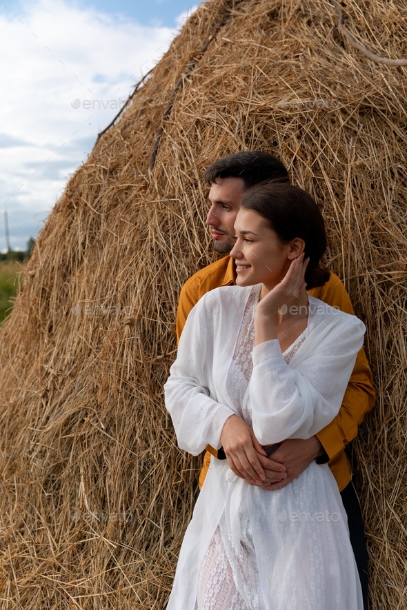 A couple stands next to haystack, love story and wedding inspiration