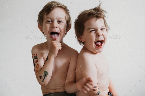  Two Toddler boy with temporary tattoos on hands playing together on flat background