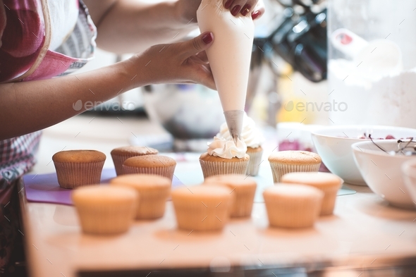 Woman making cream cheese top on cupcakes in kitchen. Cooking cakes.
