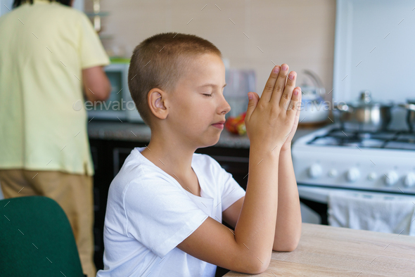 Caucasian boy prays at home at table before eating. Stay home and pray to god.