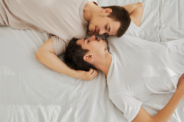 Young gay couple lying on bed head-to-toe, top view