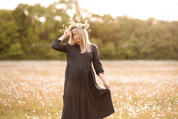 Cute pregnant woman holding belly stand in daisy meadow over nature background with flowers