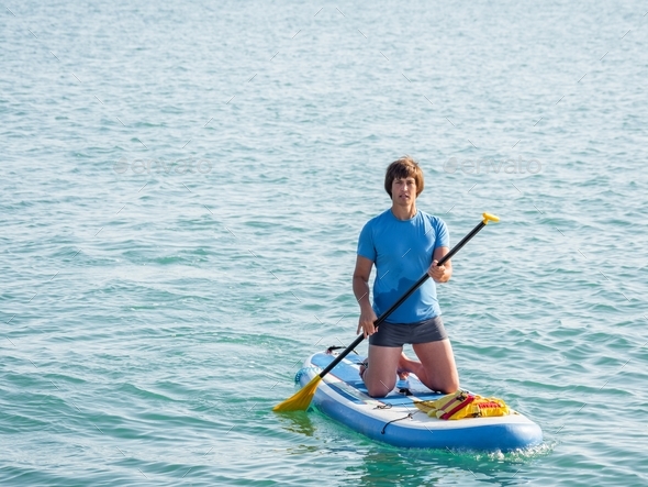 Paddle boarder. Sportsman paddling on knees on paddle board. SUP surfing. Active lifestyle.